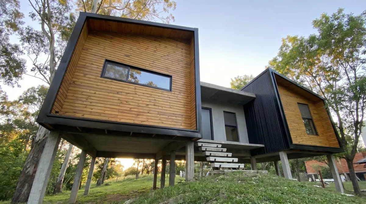 Los dos volúmenes elevados de la casa unidos por la galería de hormigón, con escalera de peldaños voladizos