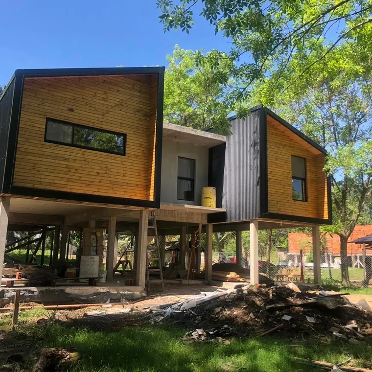 Casa en obra en Dique Luján: los dos volúmenes revestidos en madera ya apoyados sobre los pilotes de hormigón, entre los árboles