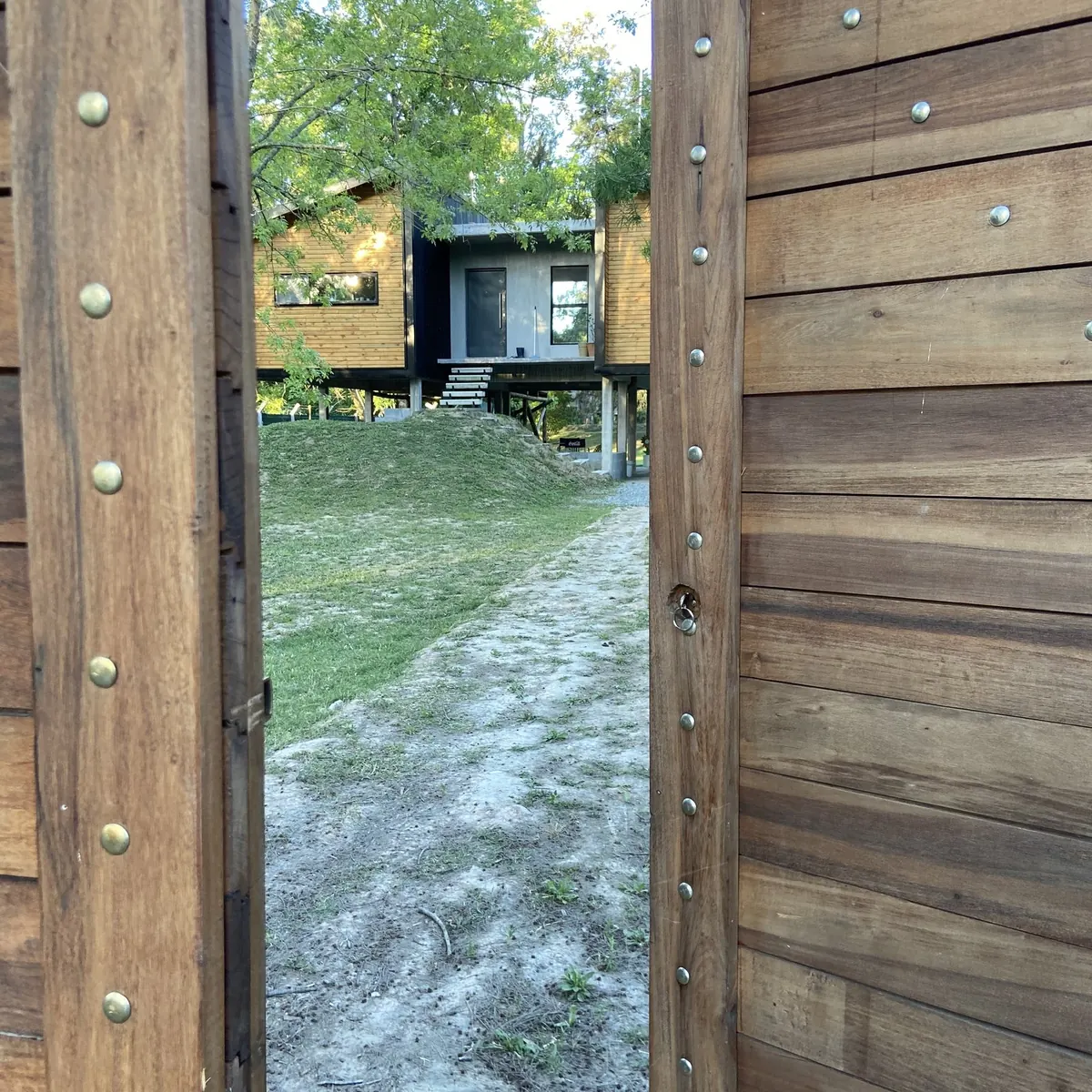 La puerta de madera maciza abierta hacia el camino de acceso, con la casa al fondo