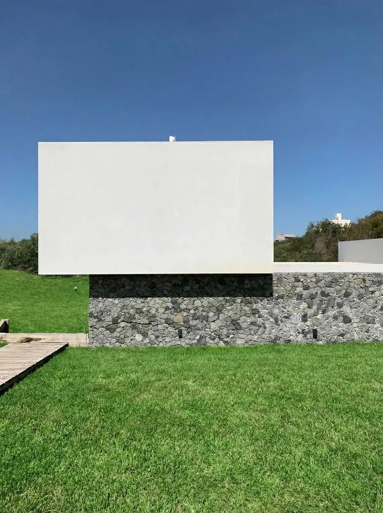 Volumen blanco en voladizo sobre el muro de piedra, desde el parque
