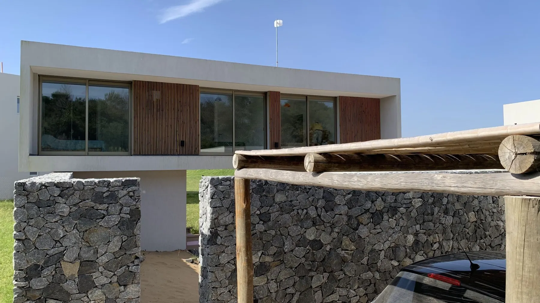 Vista desde la cochera: el volumen de vidrio y madera apoyado sobre muros de piedra