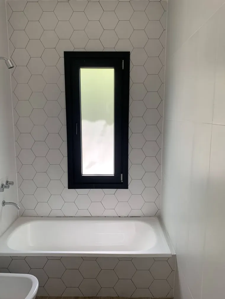Baño con revestimiento hexagonal blanco, bañera y ventana de marco negro