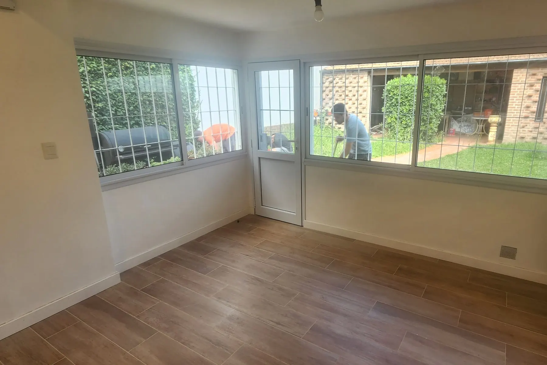 El comedor terminado en Monte Castro: ventanal en esquina con carpintería blanca, puerta al jardín y piso de porcelanato símil madera