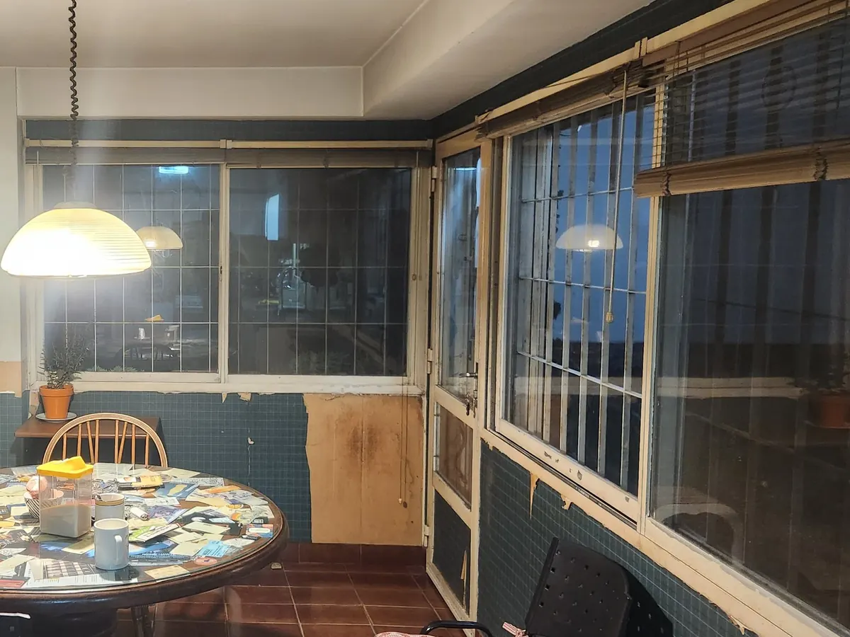 El comedor antes de la obra: azulejo verde hasta media pared, carpinterías viejas de madera y hierro con cortinas de enrollar, piso de baldosa colorada y la mesa redonda bajo la lámpara