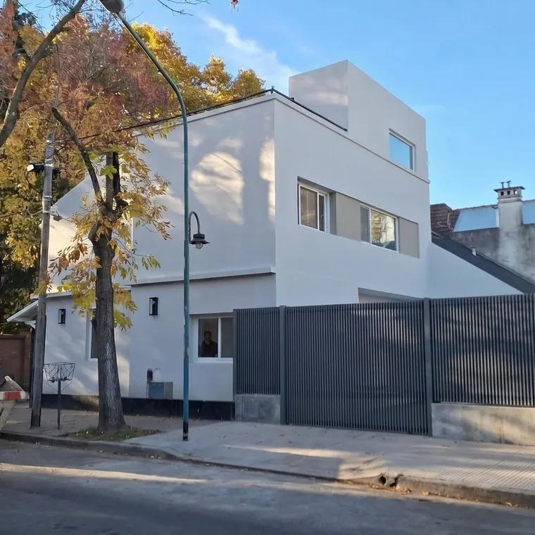 La casa terminada desde la calle: volumen blanco de dos plantas y cerco de chapa plegada oscura