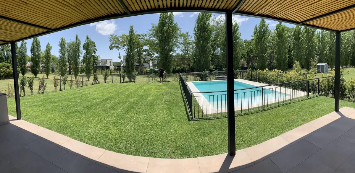 Panorámica desde la galería de una casa del estudio en Pilar: el alero de listones de madera sobre las columnas negras y el parque de lado a lado