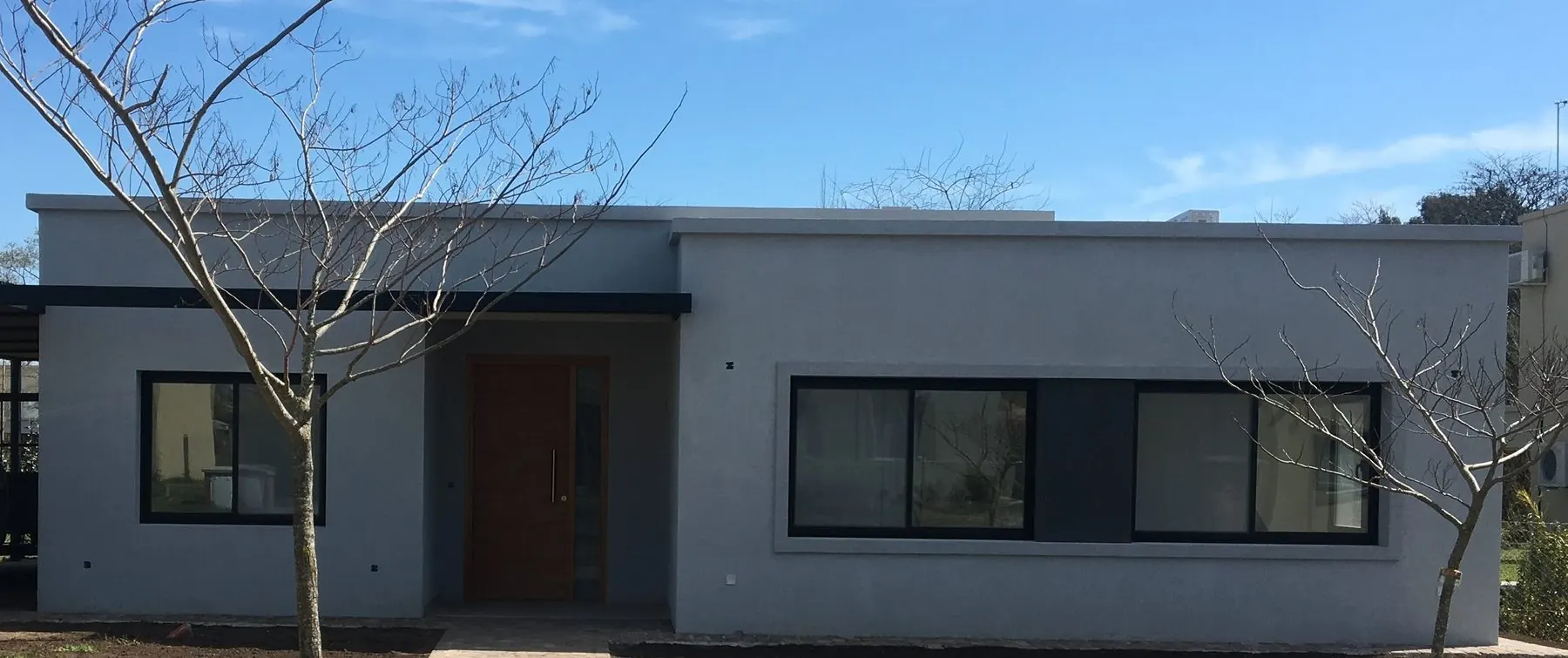 El frente sobre la calle: un plano largo y bajo con las ventanas de aluminio negro alineadas y el acceso retirado
